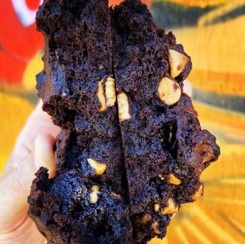 A hand holding a split chocolate muffin with chocolate chips and a rich, moist texture.