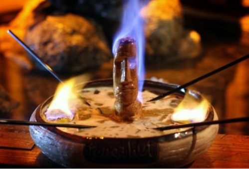 A decorative bowl with a carved figure, surrounded by flames and skewers, set against a rustic background.