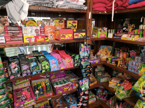 A colorful display of various candies and snacks on wooden shelves in a shop.