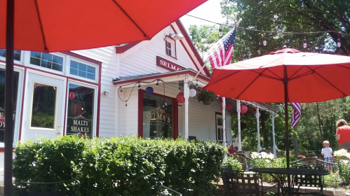 A charming white building with red umbrellas, American flags, and greenery, creating a cozy outdoor dining atmosphere.