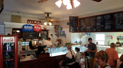 A cozy ice cream shop interior with a counter, menu board, and customers enjoying their treats.