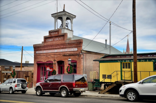 Historic brick building with a bell tower, marked "Storey County," alongside vintage train cars and festive decorations.