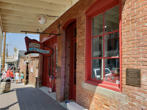 Exterior of the Comstock Firehouse Museum, featuring a red sign and brick wall, with visitors in the background.