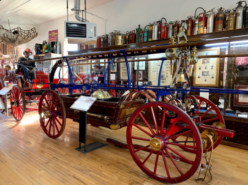 A vintage fire truck displayed in a museum, surrounded by antique fire extinguishers and historical artifacts.