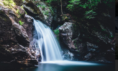 A serene waterfall cascading over rocky cliffs into a calm pool, surrounded by lush green foliage.