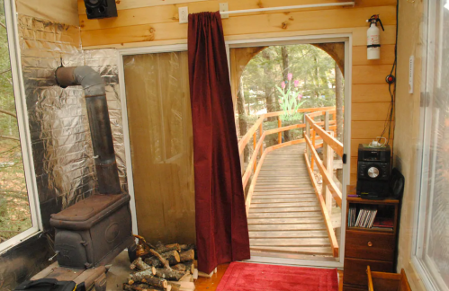 Cozy interior with a wood stove, red curtain, and a view of a wooden bridge leading outside.
