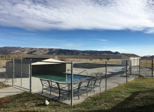 A fenced pool area with lounge chairs, surrounded by mountains and a clear blue sky.