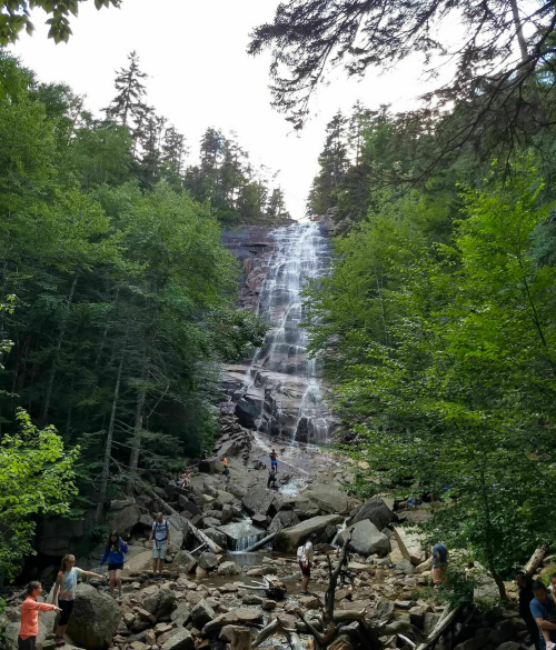 A scenic waterfall surrounded by lush greenery, with people exploring the rocky area below.