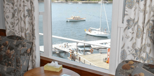 View from a window showing boats on the water, with floral curtains and a small table in the foreground.