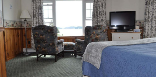 Cozy hotel room with two chairs, a TV, and a view of the water through large windows.