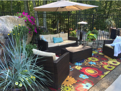 Cozy outdoor seating area with a patio umbrella, colorful rug, and vibrant flowers in a lush garden setting.