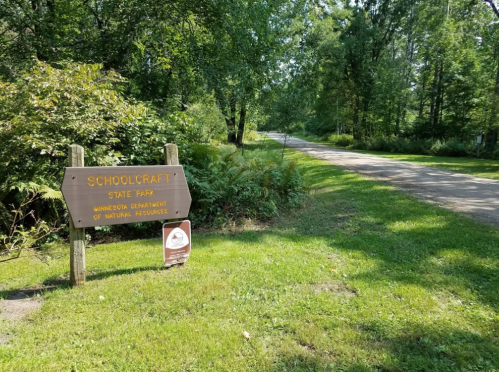 Sign for Schoolcraft State Park in Minnesota, with a gravel path and lush greenery in the background.