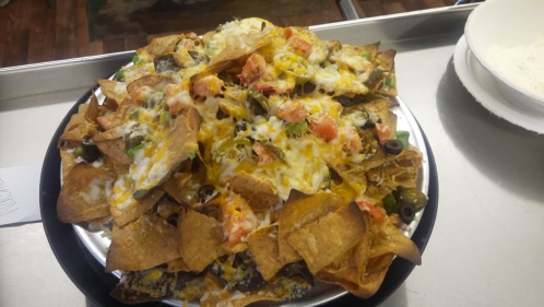 A large plate of nachos topped with melted cheese, tomatoes, olives, and jalapeños.