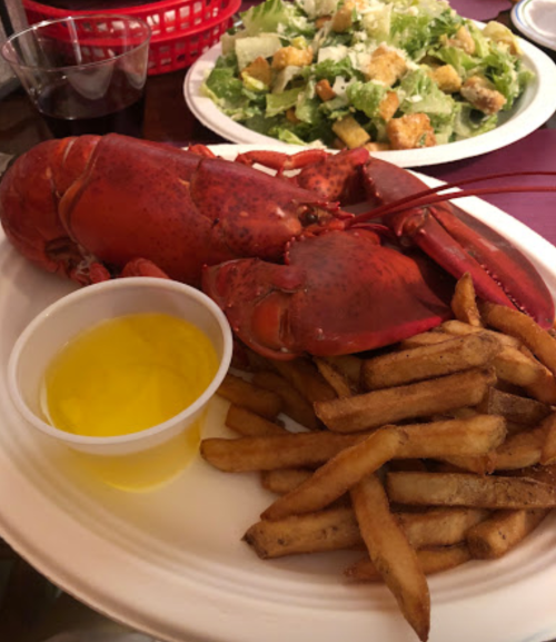 A plate with a whole lobster, a side of fries, and a small cup of melted butter, with a salad in the background.
