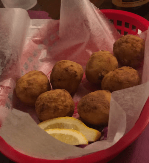 A red basket lined with paper holds eight golden-brown fried balls and two lemon wedges.