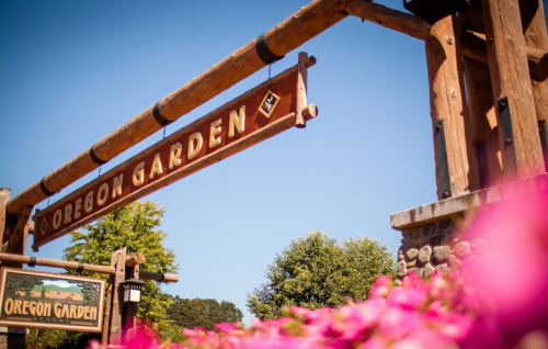 Sign for Oregon Garden Resort with wooden beams and vibrant flowers in the foreground against a clear blue sky.