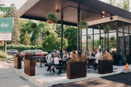 A group of people dining at an outdoor restaurant with greenery and modern decor on a sunny day.