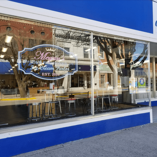 A storefront with large windows displaying "Maggie's Ice Cream Parlor" sign and empty seating inside.