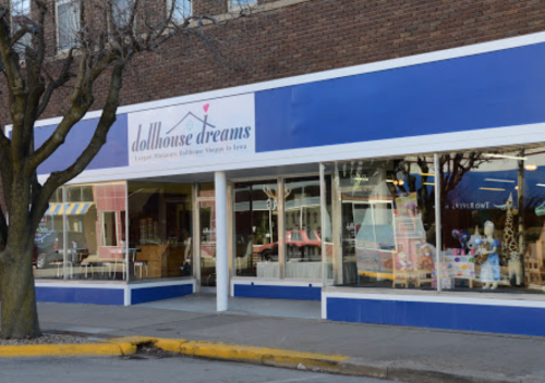 Storefront of "Dollhouse Dreams," a dollhouse shop in Iowa, featuring large windows and a blue exterior.