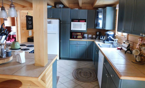 Cozy kitchen with wooden beams, blue cabinets, a white fridge, and a tiled countertop, featuring various appliances.