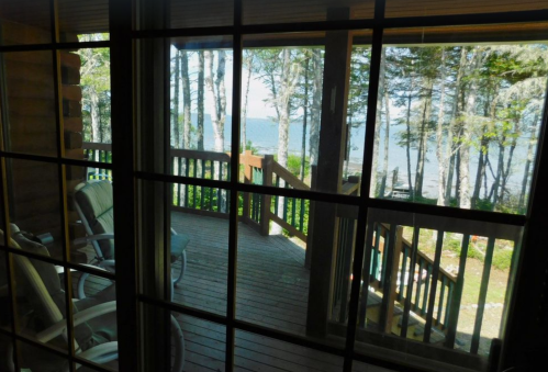 View from a cabin window showing a wooden deck and trees overlooking a serene lake.