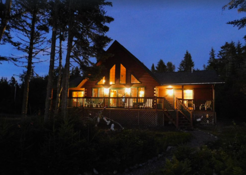 A cozy log cabin illuminated at dusk, surrounded by trees and a peaceful landscape.