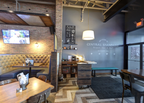 Interior of a restaurant featuring a cozy seating area, a bar, and a wall with the name "Central Standard."
