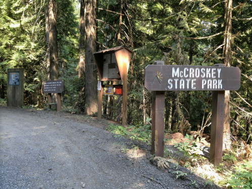 Entrance to McCroskey State Park, featuring wooden signs and a gravel path surrounded by tall trees.