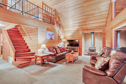 Cozy living room with wooden walls, a staircase, leather sofas, a TV, and a fireplace, creating a warm atmosphere.