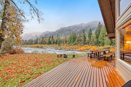 Scenic view of a river and mountains surrounded by autumn foliage, with a wooden deck and picnic area in the foreground.