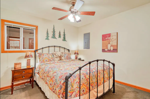 Cozy bedroom with a metal bed frame, colorful patterned bedding, wooden nightstands, and decorative wall art.