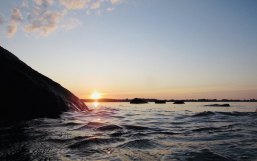 A serene sunset over calm waters, with rocks silhouetted against the colorful sky.