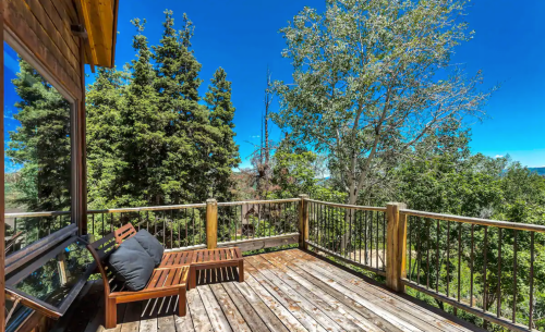 A wooden deck with lounge chairs surrounded by tall trees and a clear blue sky.
