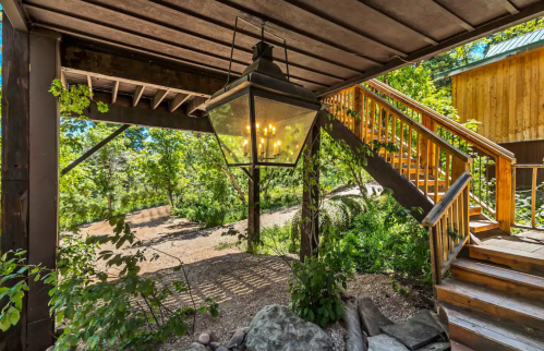 A rustic outdoor area featuring a large lantern, wooden stairs, and lush greenery surrounding a gravel path.