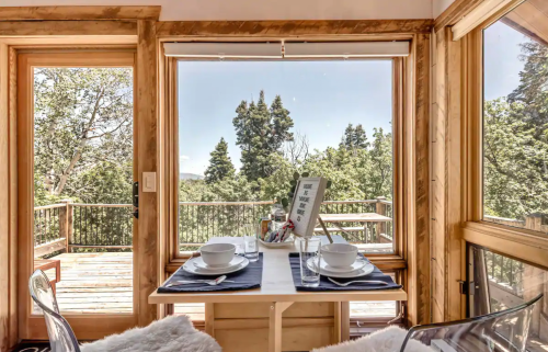 Cozy dining area with a table set for two, featuring large windows overlooking a forested view.