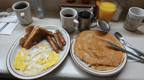 A breakfast plate with eggs, sausage, toast, and a large pancake, accompanied by coffee and orange juice.