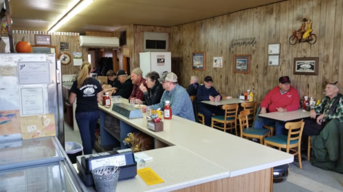 A cozy diner interior with patrons seated at the counter and tables, enjoying meals and chatting.