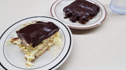 Two plates with dessert: one has a layered cake with cream and chocolate icing, the other is a chocolate-covered treat.