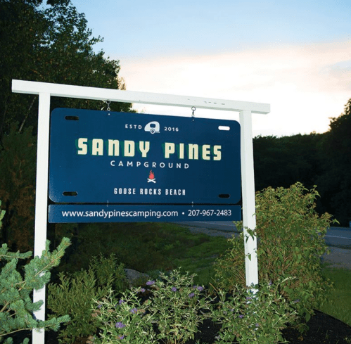 Sign for Sandy Pines Campground, established in 2016, located near Goose Rocks Beach, with contact information.