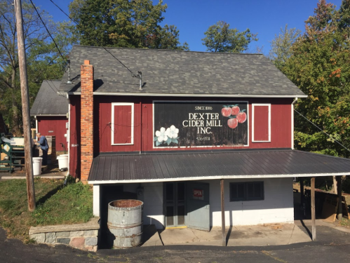 A red barn-style building with a sign for Dexter Cider Mill, surrounded by trees and a clear blue sky.