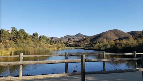 A serene landscape featuring a calm lake surrounded by hills and greenery under a clear blue sky.