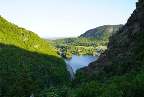 A scenic view of a lush green valley with a river, mountains, and a small town in the distance under a clear blue sky.