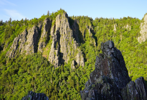 A rugged mountain landscape with steep cliffs and lush green trees under a clear blue sky.