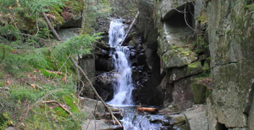 A serene waterfall cascading through rocky terrain, surrounded by lush greenery and moss-covered stones.
