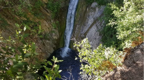 A waterfall cascading into a dark pool, surrounded by rocky cliffs and lush greenery.