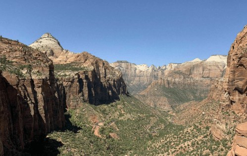 A panoramic view of Zion National Park, showcasing towering red rock cliffs and a clear blue sky.