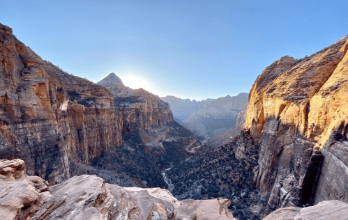 A breathtaking view of a canyon at sunrise, with steep rock formations and a winding path below.