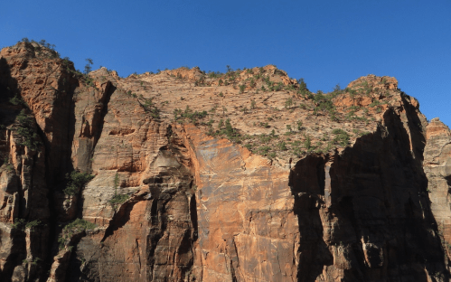 A rugged rock formation with steep cliffs and sparse vegetation under a clear blue sky.
