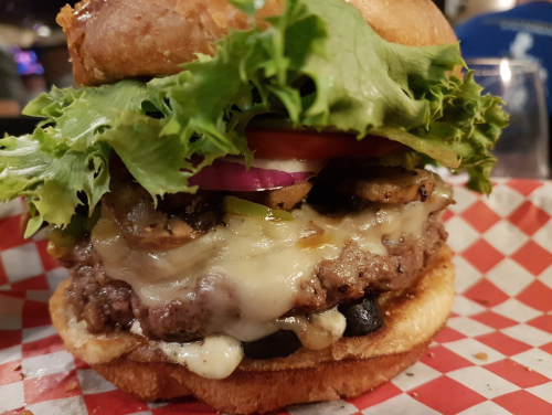 A juicy burger with melted cheese, lettuce, tomato, onions, and mushrooms on a toasted bun, served on a checkered paper.