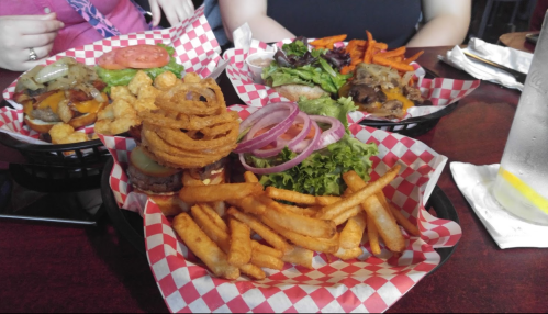 Three plates of burgers with fries, onion rings, and salads, served in red and white checkered baskets.